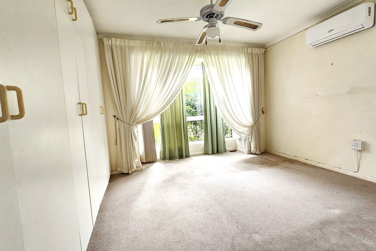 A spacious bedroom featuring built-in cupboards, a ceiling fan, and a wall-mounted air conditioning unit, offering a blank canvas for renovation.