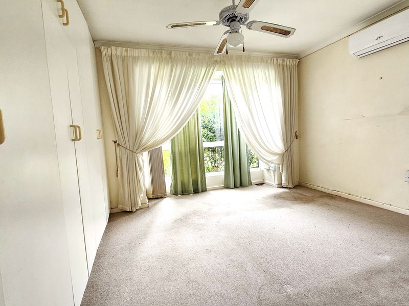 A spacious bedroom featuring built-in cupboards, a ceiling fan, and a wall-mounted air conditioning unit, offering a blank canvas for renovation.