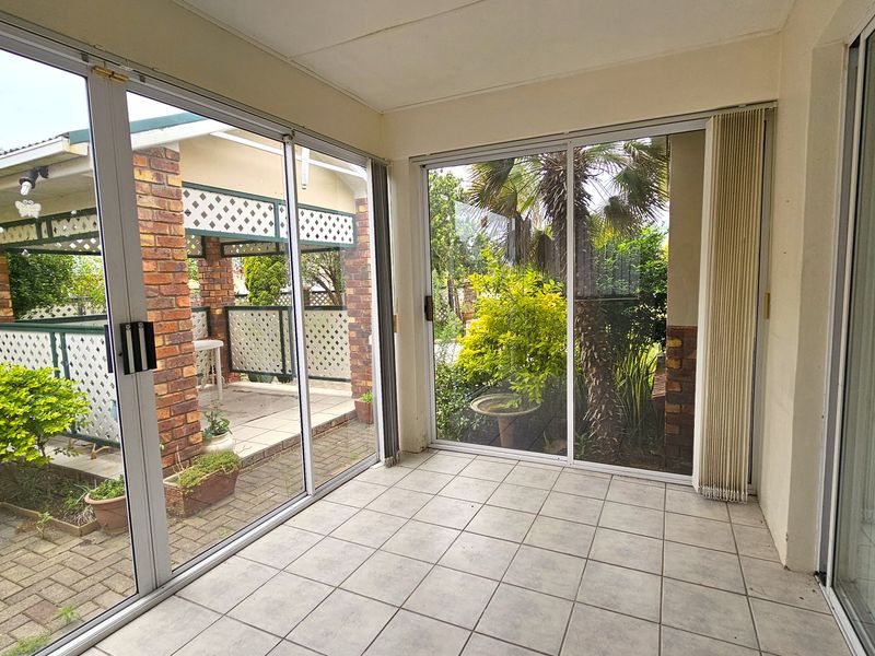A bright, enclosed patio area featuring tiled flooring and large sliding glass doors that provide views of the garden and outdoor entertainment space.