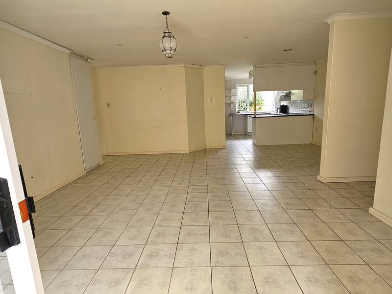 An open-plan living and kitchen area featuring tiled flooring, neutral walls, and direct access to an outdoor space through a sliding glass door.