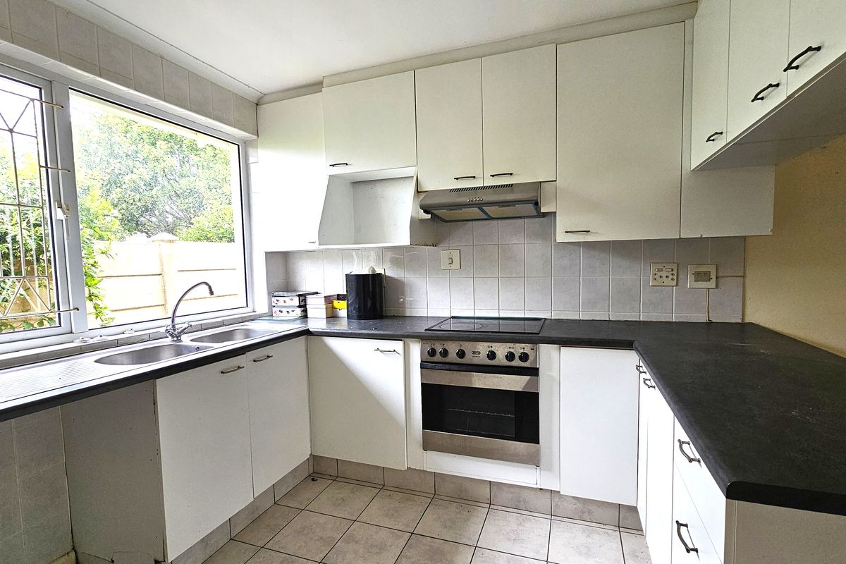 Functional kitchen featuring white cabinetry, dark laminate countertops, built-in oven with hob, extractor fan, and tiled flooring with a large window overlooking the garden.