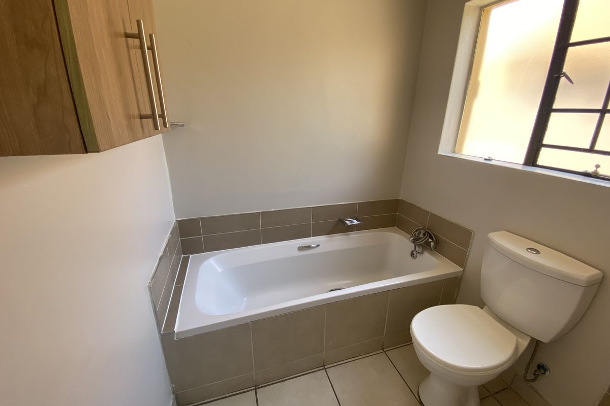 A functional bathroom featuring a built-in bathtub with tiled surround, a standard toilet, and a wall-mounted wooden storage cabinet.