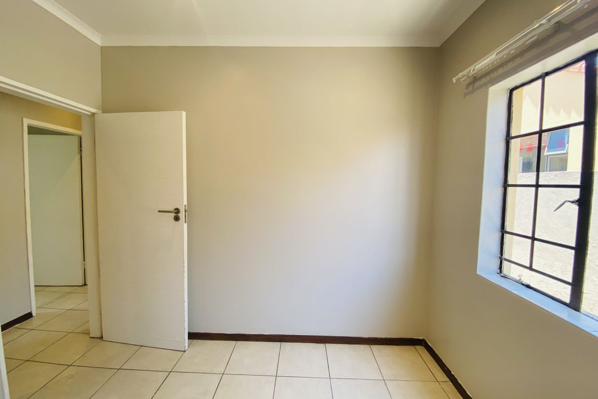 A bright, empty bedroom featuring neutral wall paint, tiled flooring, and a window with security bars.