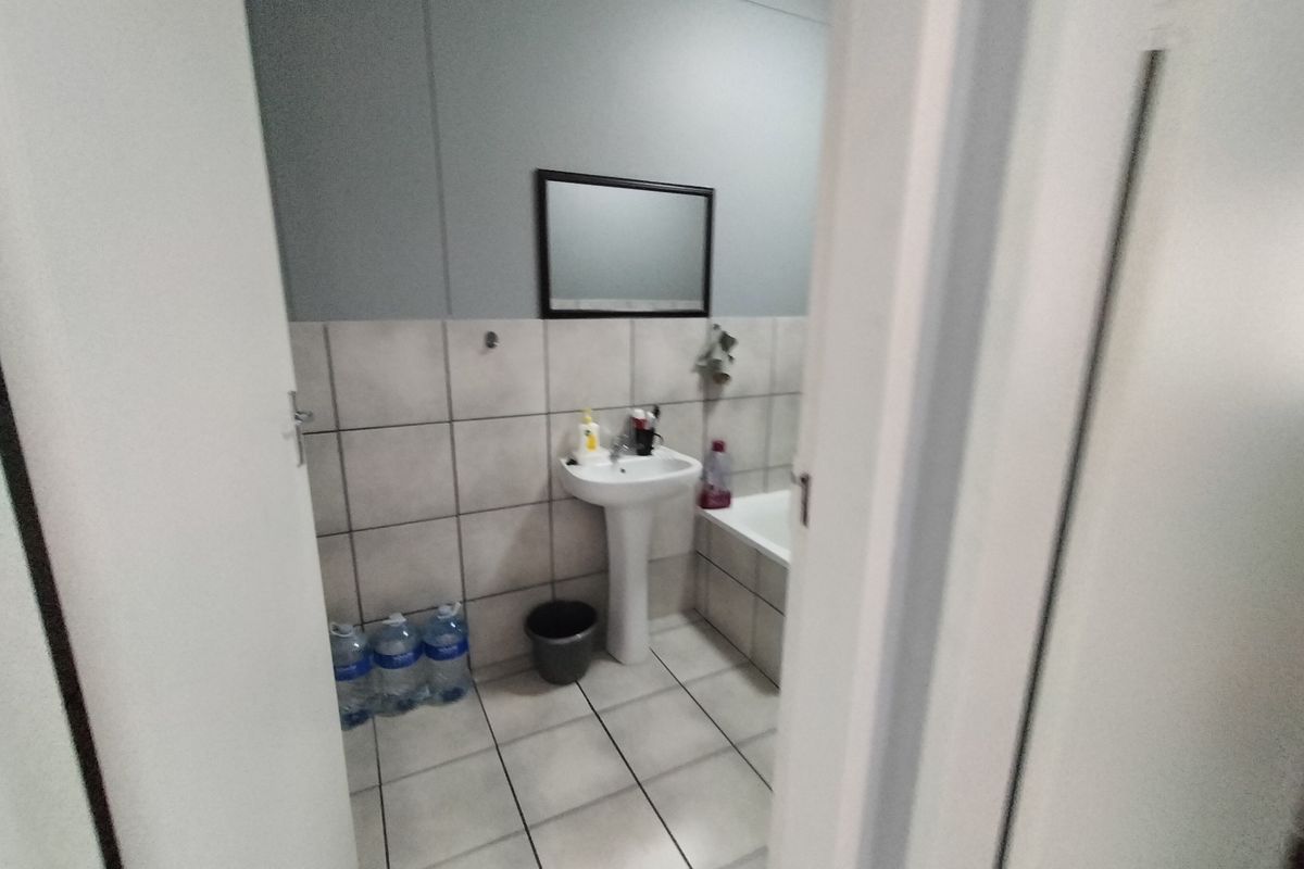 A functional bathroom featuring a pedestal basin, bathtub, and neutral wall and floor tiling.