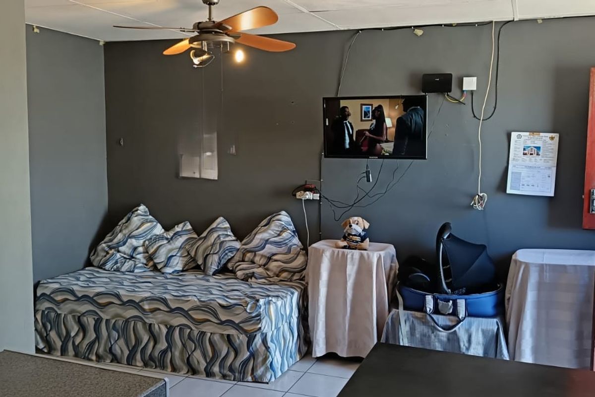 A living area featuring tiled flooring, a ceiling fan, and a timber door, currently requiring cosmetic updates and better cable management.
