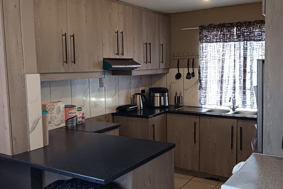 A functional kitchen featuring modern wood-look laminate cabinetry, dark countertops, a stainless steel sink, and a tiled backsplash with an integrated extractor fan.