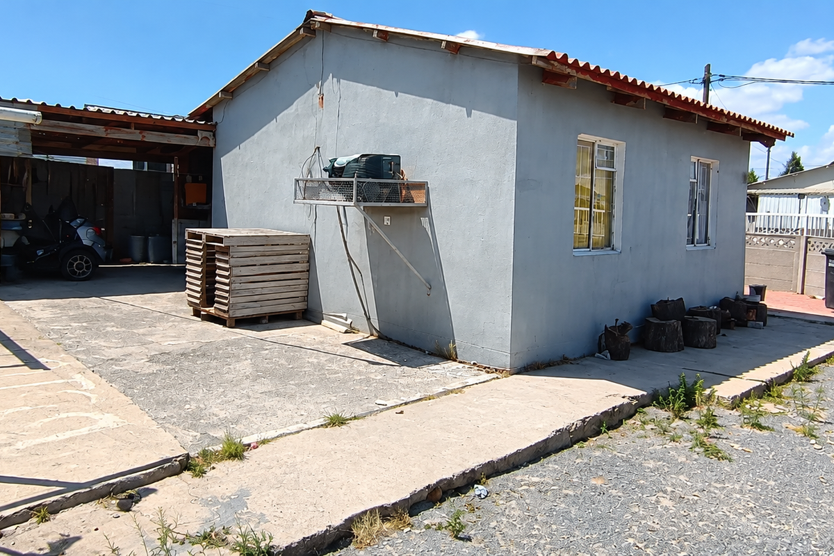 Rear exterior view of the property featuring a concrete patio area, covered carport, and perimeter boundary walling.