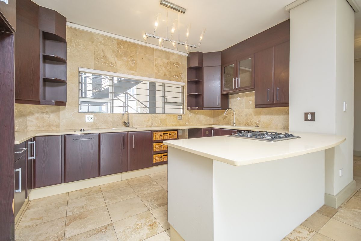 A well-appointed kitchen featuring dark wood cabinetry, stone tile backsplash, a central island with a gas hob, and ample counter space.