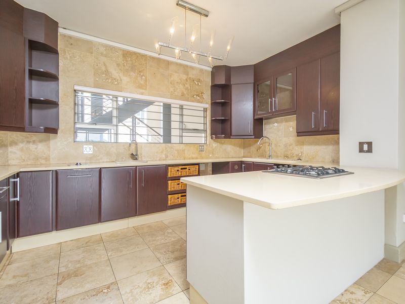 A well-appointed kitchen featuring dark wood cabinetry, stone tile backsplash, a central island with a gas hob, and ample counter space.