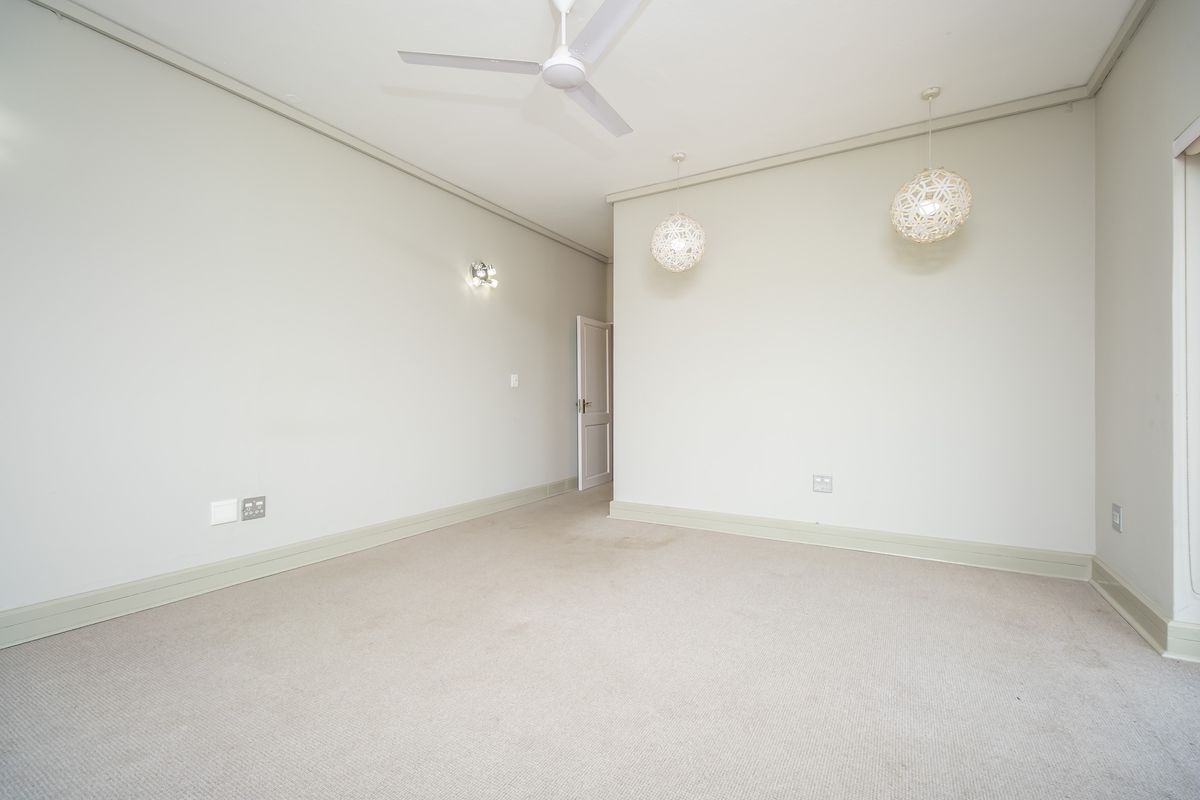 A spacious, empty bedroom featuring neutral carpeting, a ceiling fan, and modern pendant lighting, providing a clean and versatile canvas for personalization.