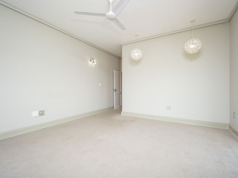 A spacious, empty bedroom featuring neutral carpeting, a ceiling fan, and modern pendant lighting, providing a clean and versatile canvas for personalization.