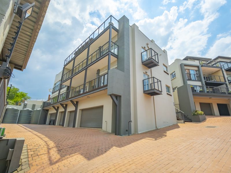 Modern apartment complex exterior featuring paved driveway, multiple roller shutter garage doors, and private balconies with metal railings.