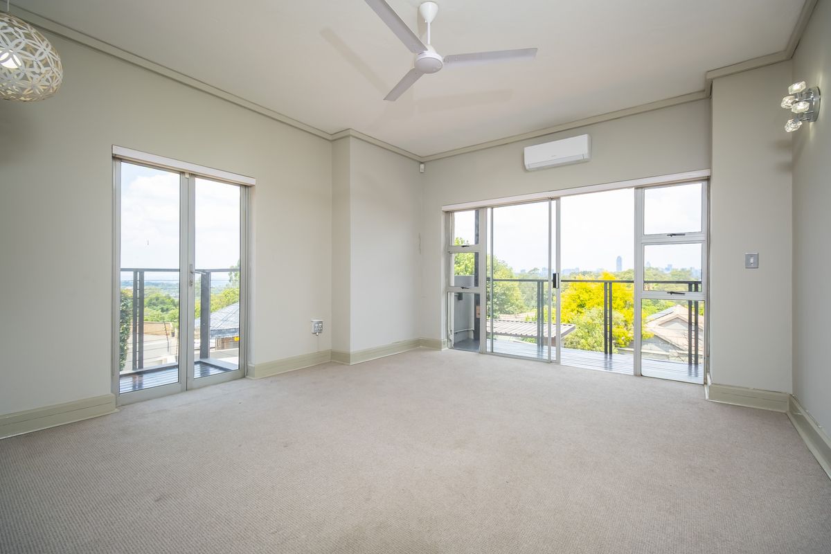 Spacious, light-filled living area featuring neutral carpeting, a ceiling fan, air conditioning, and dual sliding glass doors opening onto a balcony with scenic views.