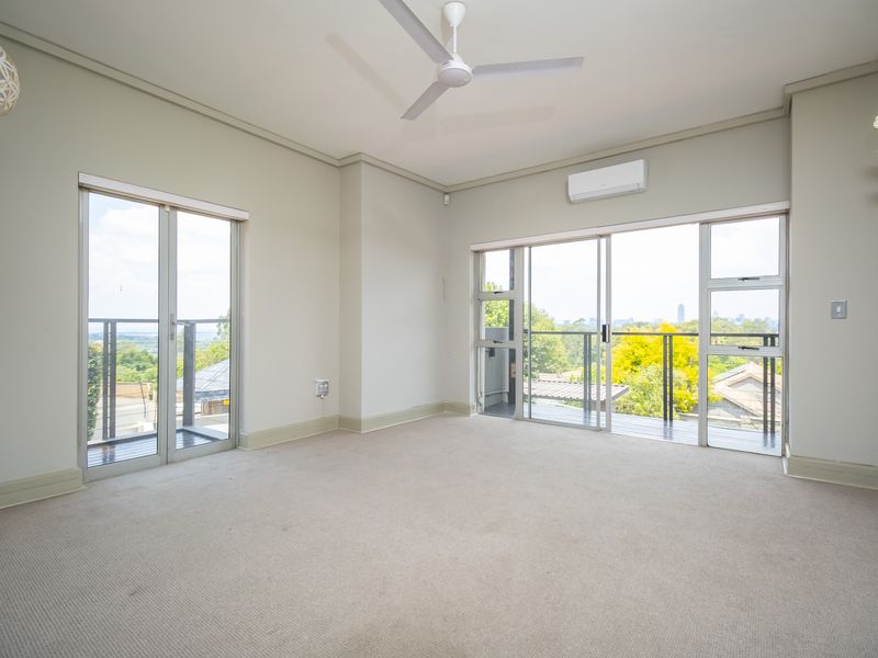 Spacious, light-filled living area featuring neutral carpeting, a ceiling fan, air conditioning, and dual sliding glass doors opening onto a balcony with scenic views.