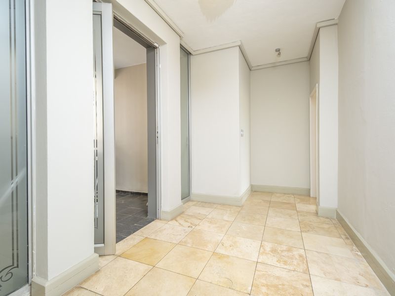 A bright, empty hallway featuring neutral tiled flooring and clean wall finishes, providing a versatile transition space within the apartment.