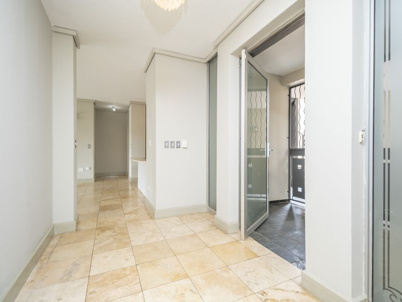 A bright and spacious hallway featuring neutral wall tones and elegant travertine floor tiles, leading towards an open-plan living area and exterior access.