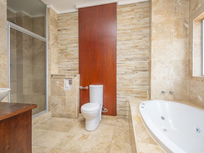 Modern bathroom featuring travertine wall and floor tiles, a built-in jetted bathtub, a glass-enclosed shower, and a stone feature wall.
