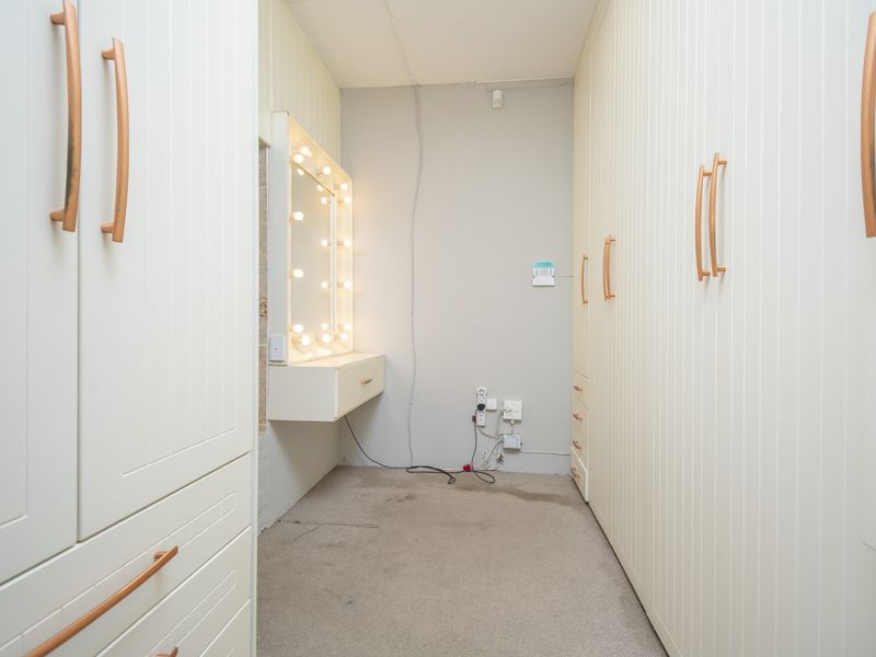 A walk-in dressing area featuring extensive built-in cabinetry, a vanity station with integrated lighting, and carpeted flooring.