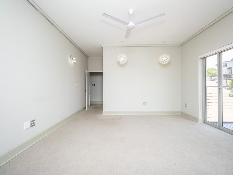 A spacious, empty living room featuring neutral carpeting, a ceiling fan, and sliding glass doors that provide access to an outdoor area.
