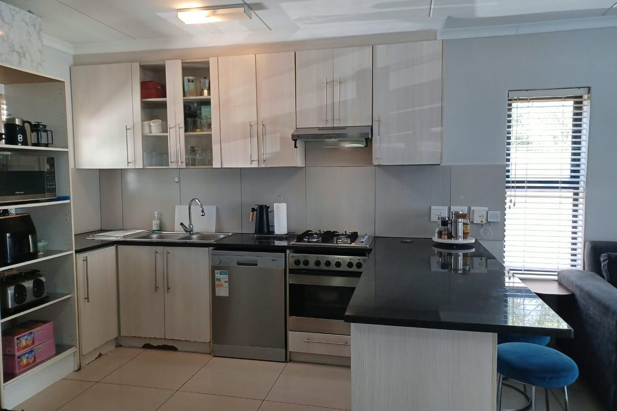 Modern kitchen featuring light-toned cabinetry, granite countertops, gas hob, and integrated appliances, with a breakfast bar area.