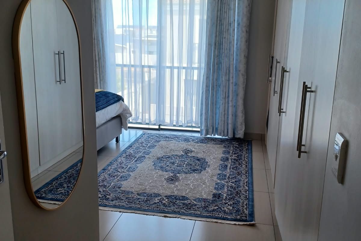 A well-maintained bedroom featuring built-in cupboards, tiled flooring, and a sliding glass door leading to a balcony.