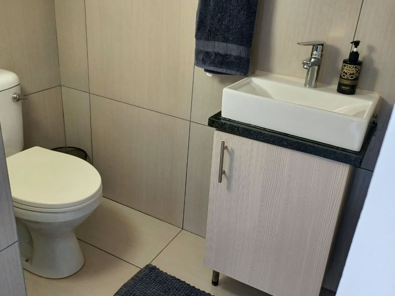 A compact bathroom featuring a modern vessel sink on a vanity cabinet, a toilet, and neutral wall and floor tiling.