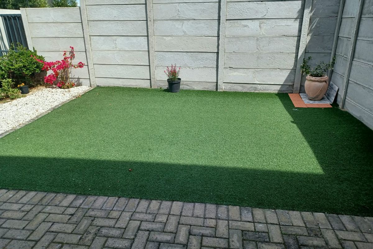 A low-maintenance rear courtyard featuring a paved patio area and a neat artificial turf lawn enclosed by precast concrete boundary walls.