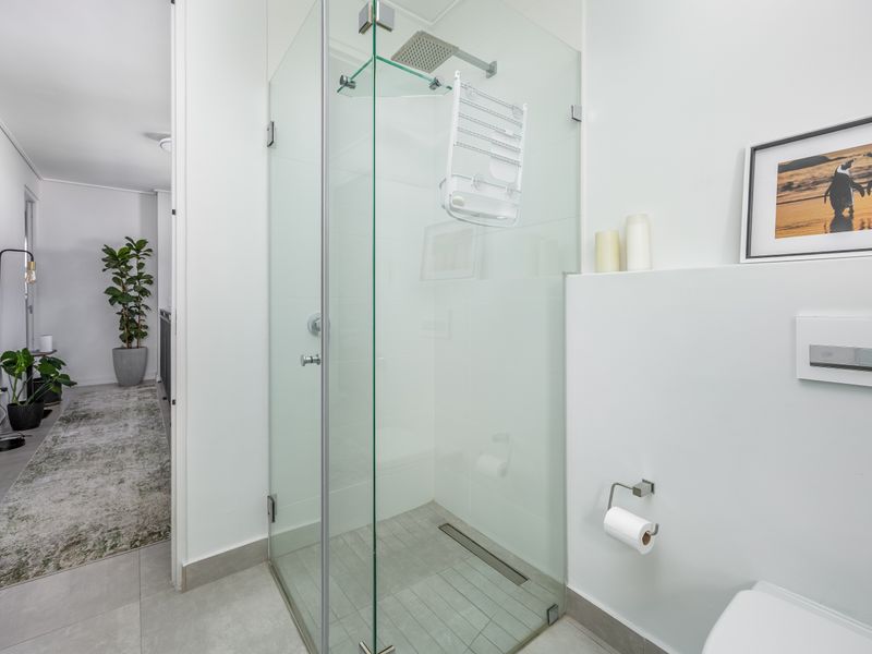 Modern bathroom featuring a sleek glass-enclosed walk-in shower with a rain shower head and contemporary wall-mounted toilet flush plate.