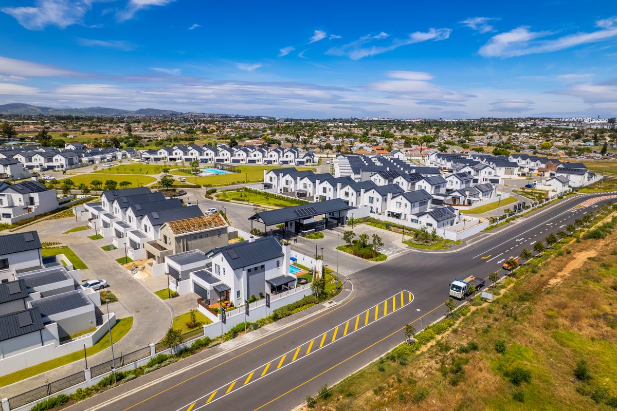 Aerial view of a modern residential estate featuring multiple townhouses, paved internal roads, a security gatehouse, and communal recreational facilities.