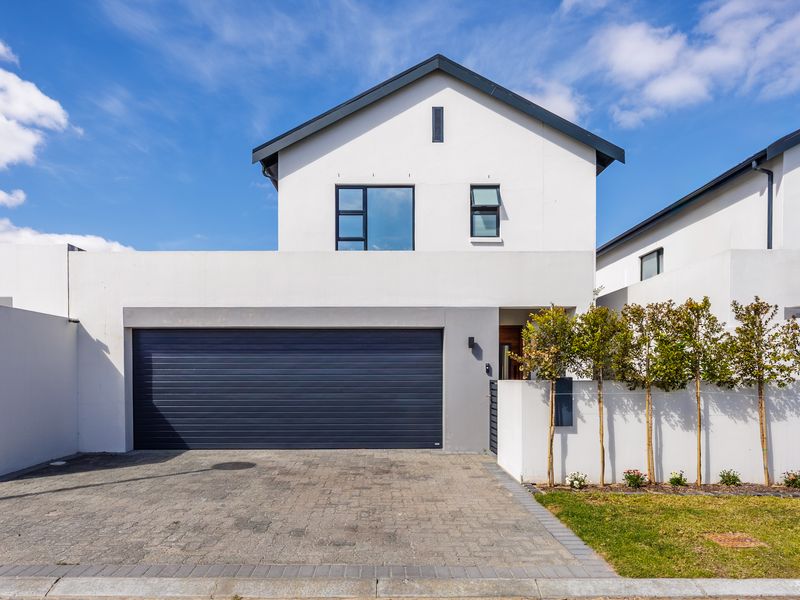 Modern double-storey residential property featuring a clean white facade, dark grey garage door, paved driveway, and manicured landscaping.