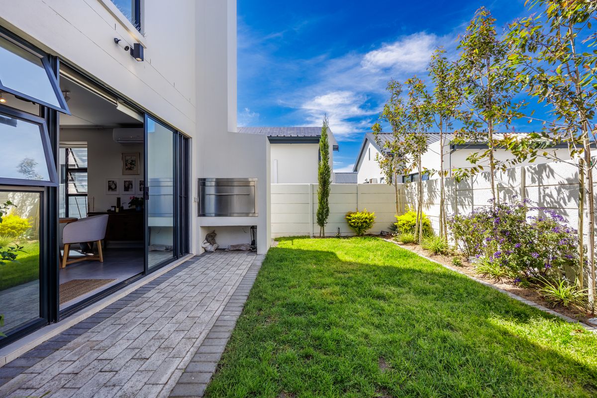 A well-maintained rear garden featuring a paved walkway, a built-in braai, and a neat lawn, seamlessly connected to the interior via sliding glass doors.