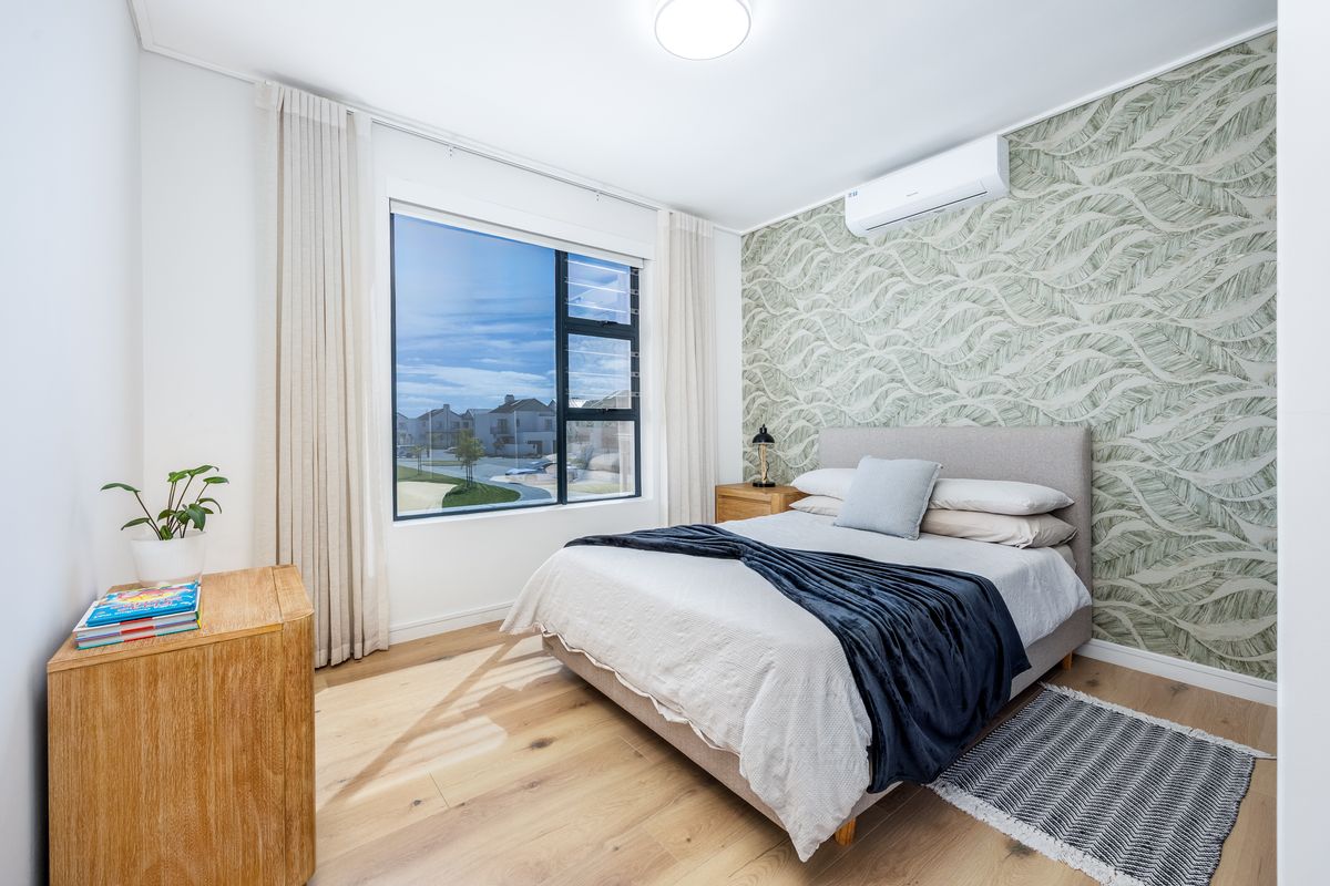 A bright and modern bedroom featuring timber flooring, a decorative feature wall, and a wall-mounted split-system air conditioner.