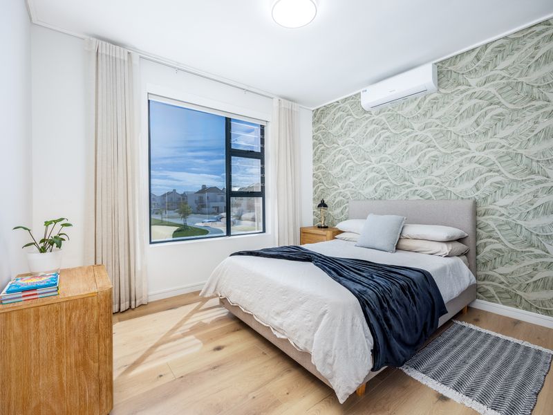 A bright and modern bedroom featuring timber flooring, a decorative feature wall, and a wall-mounted split-system air conditioner.