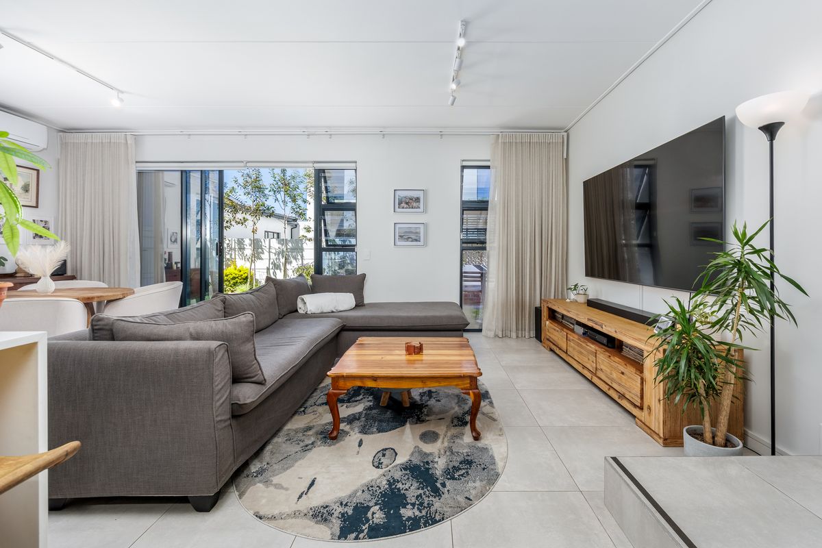 A bright and spacious living room featuring large sliding glass doors, neutral tiled flooring, and modern track lighting, creating a comfortable and inviting atmosphere.