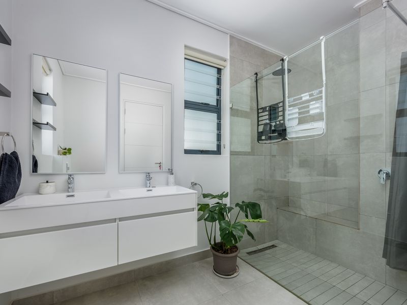 Modern bathroom featuring a sleek double vanity with wall-mounted cabinetry and a spacious walk-in shower with a glass screen and rain shower head.