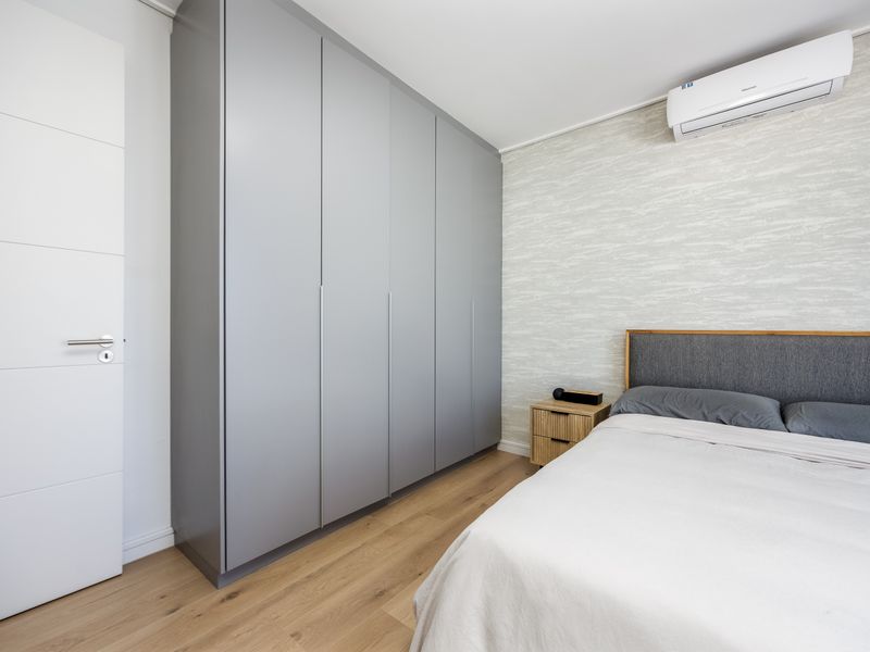 Modern bedroom featuring light wood-look flooring, a large grey built-in wardrobe, textured feature wall, and a wall-mounted air conditioning unit.
