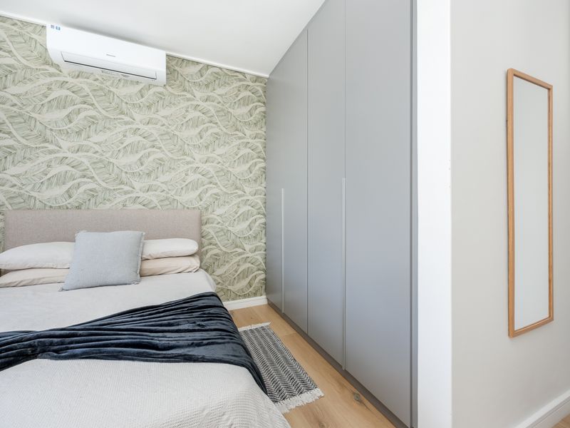 A well-maintained bedroom featuring modern built-in wardrobes, timber flooring, a split-system air conditioner, and stylish feature wallpaper.