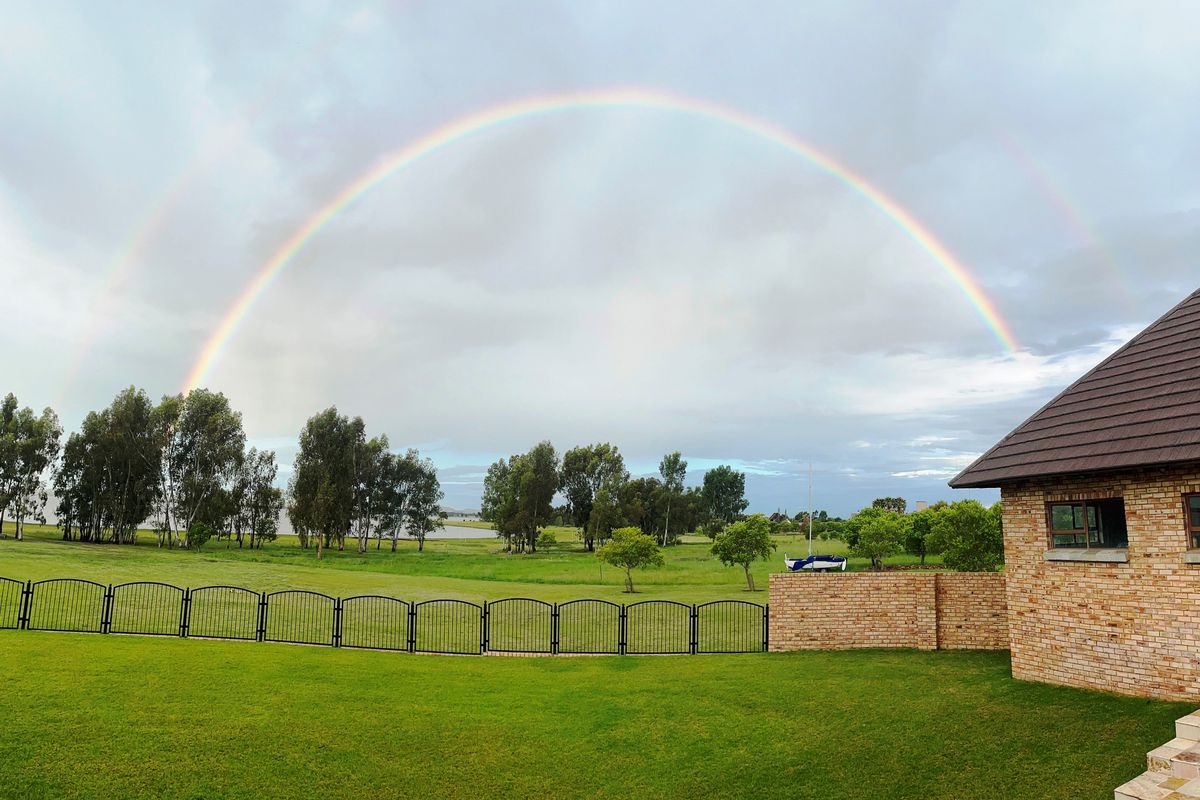 A scenic rear view of the property featuring a well-maintained lawn, brick wall, and metal fencing under a double rainbow.