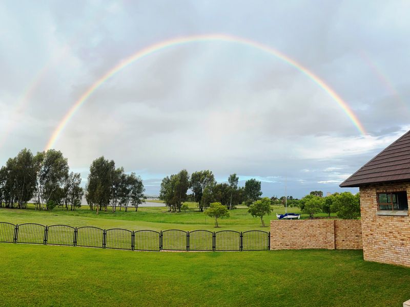 A scenic rear view of the property featuring a well-maintained lawn, brick wall, and metal fencing under a double rainbow.