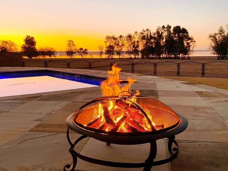 Outdoor pool area featuring stone paving and metal perimeter fencing, overlooking a scenic landscape at sunset.