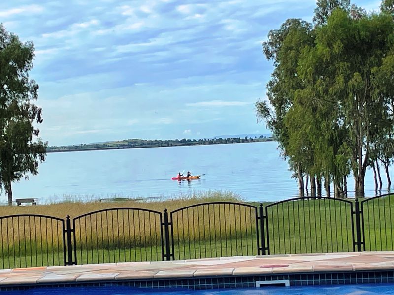 Scenic view overlooking a large dam or lake, featuring a swimming pool with wrought iron fencing and paved surround in the foreground.