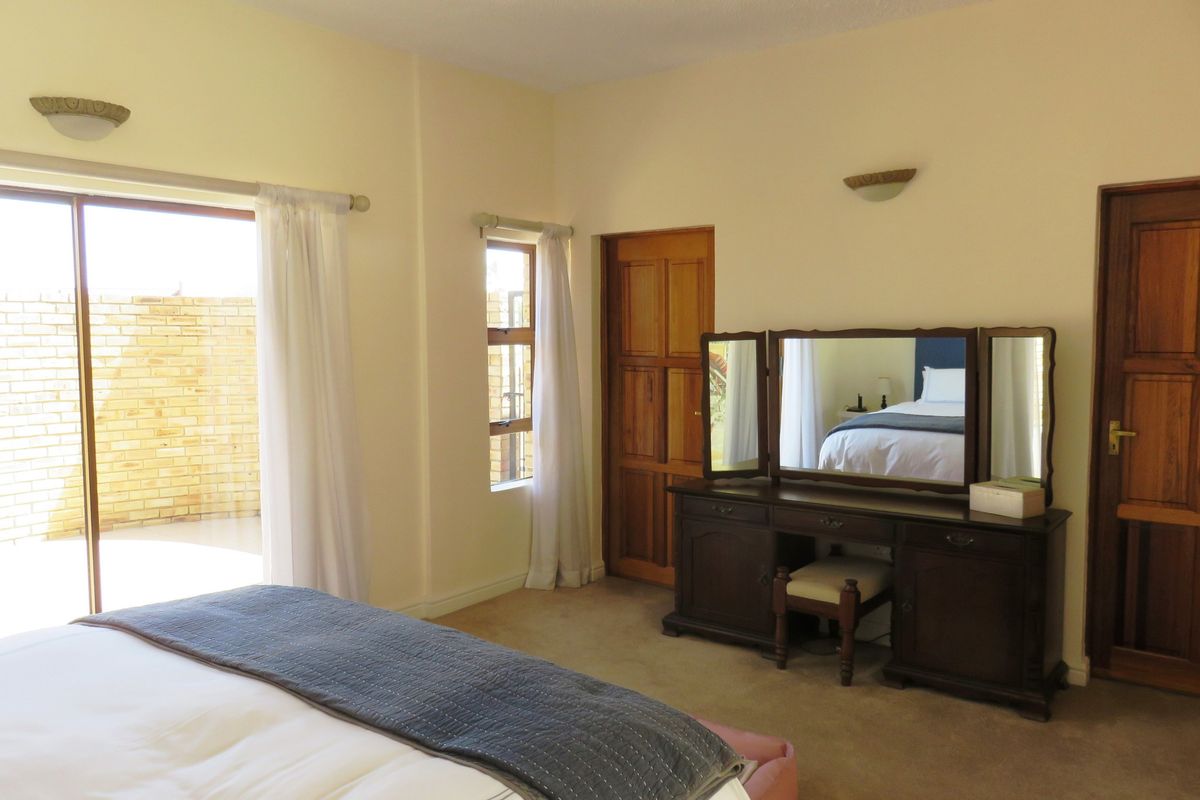 Spacious bedroom featuring carpeted flooring, wall-mounted lighting, and direct access to an outdoor patio area through a sliding glass door.