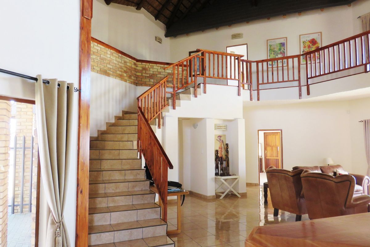 Spacious living area featuring a prominent tiled staircase with wooden balustrades, high thatched ceilings with exposed rafters, and a mezzanine landing.