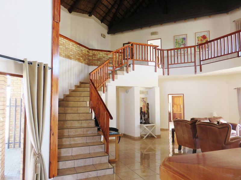 Spacious living area featuring a prominent tiled staircase with wooden balustrades, high thatched ceilings with exposed rafters, and a mezzanine landing.