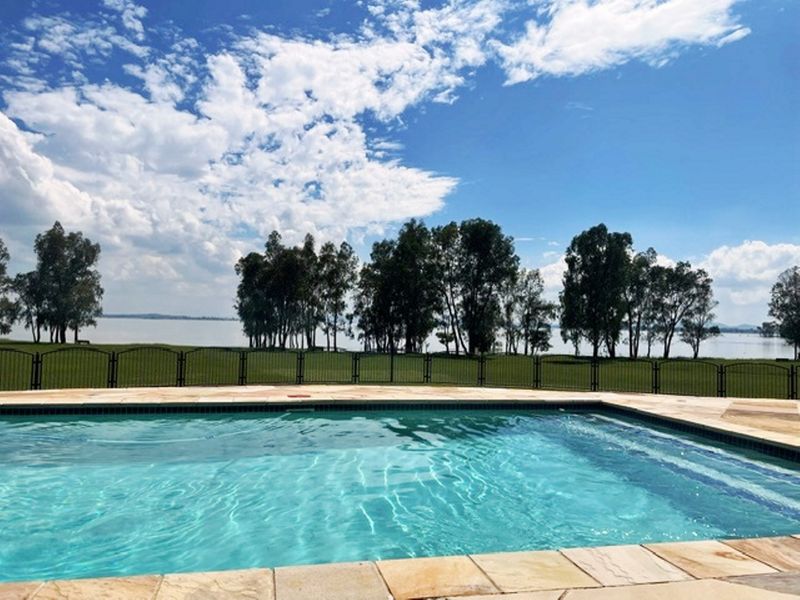 A well-maintained swimming pool with stone coping, featuring a metal perimeter fence and scenic views of the surrounding landscape and water.