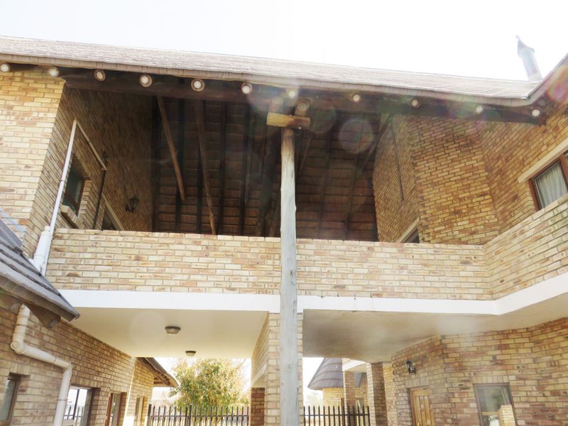 A view of the rear exterior featuring a face brick facade, a covered patio area, and exposed timber roof trusses under a thatched roof.