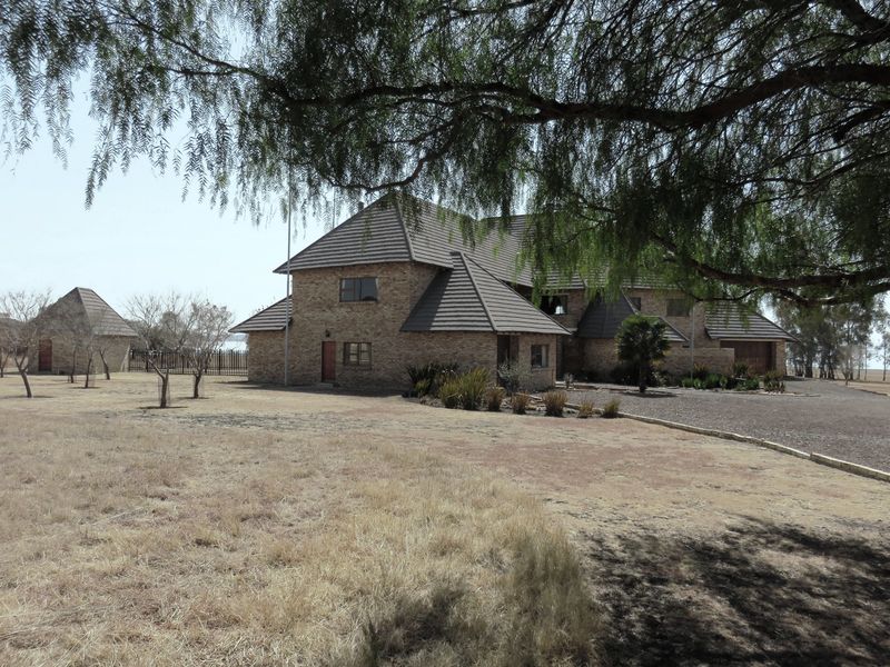 A view of the main face-brick residence and a detached outbuilding, set on a large plot with a gravel driveway and mature trees.