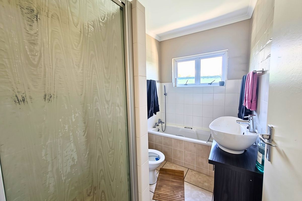 A functional bathroom featuring a shower enclosure, bathtub, toilet, and a modern vessel sink set on a vanity cabinet with tiled finishes.