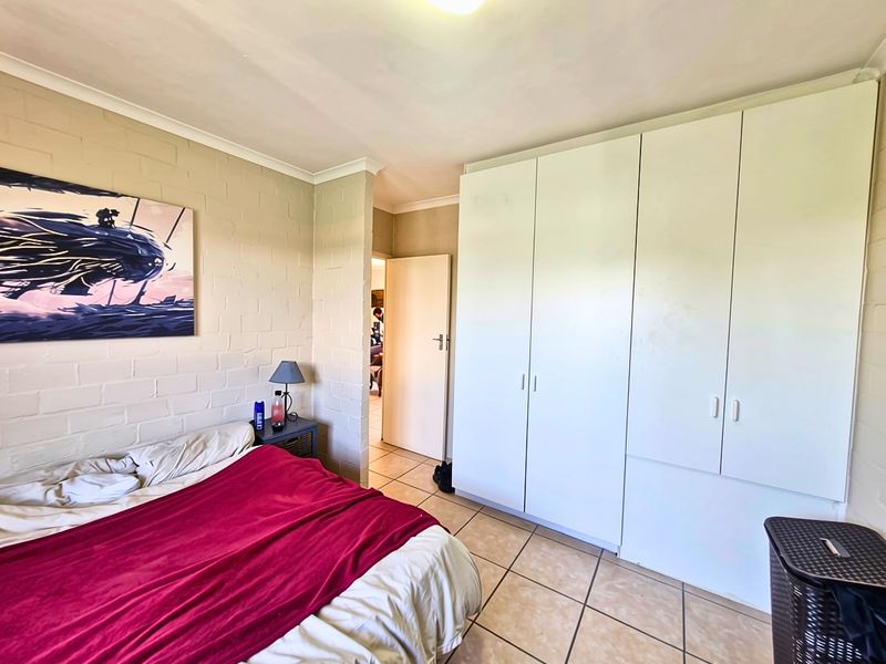 A bedroom featuring tiled flooring, coved ceilings, and built-in cupboards, offering a functional space with potential for cosmetic updates.