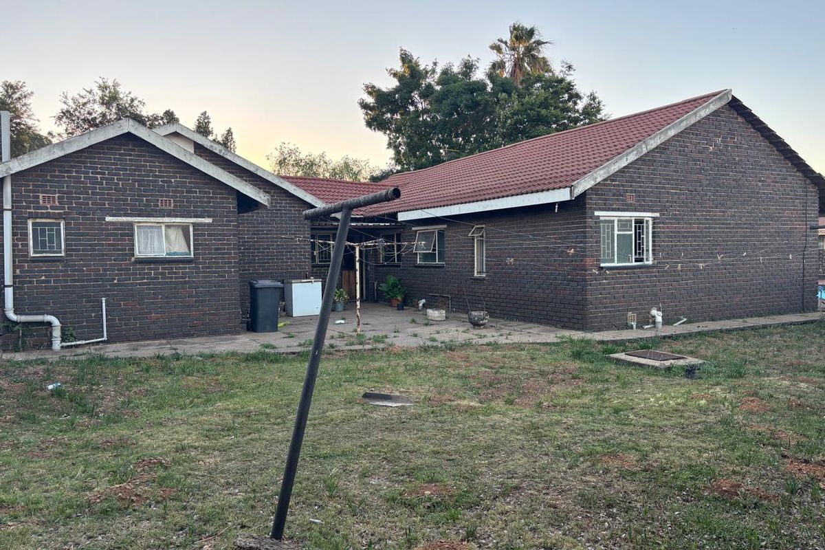 Rear view of a brick house featuring a tiled roof, paved patio area, and a large backyard with established garden space.